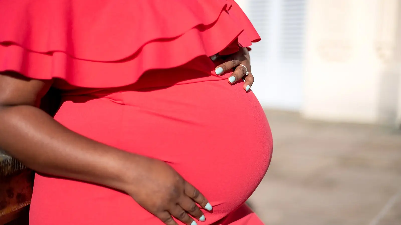 A pregnant woman in a red dress, resting her hands on her bump