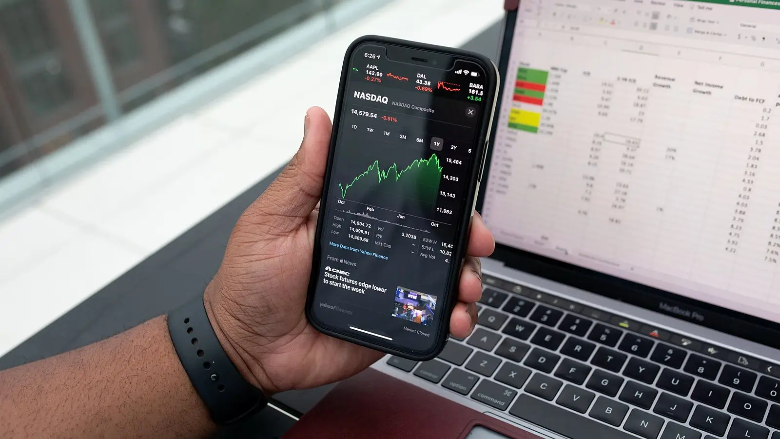 Checking figures on a phone beside a spreadsheet on a laptop