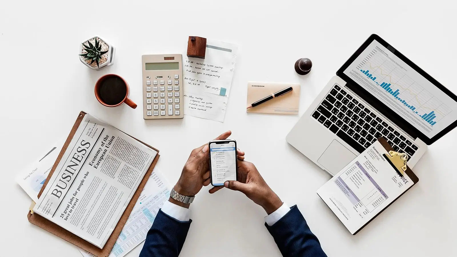 A desk seen from above with a calculator, laptop, phone and tax papers