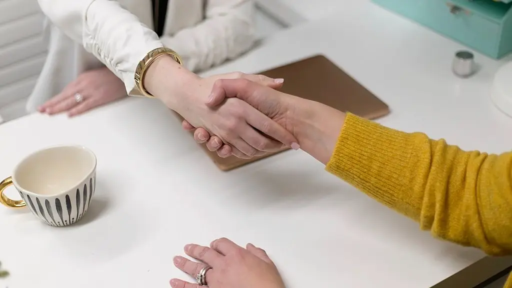 Two people shaking hands across a desk to close an agreement